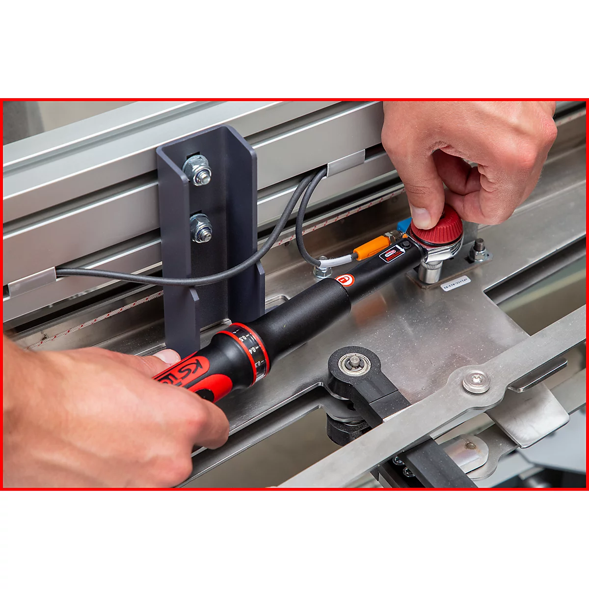 Hände bedienen Knarre. Schwarzer Griff, roter Akzent, silberfarbener Hintergrund. Montage von Bauteilen.